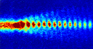 Protonenbündel im Takt: Der Zugstrahl aus kleinen Protonenpaketen durchquert das Plasmafeld. Damit bildet sich eine Welle, auf der sich Elektronen beschleunigen lassen. (Bild: AWAKE)